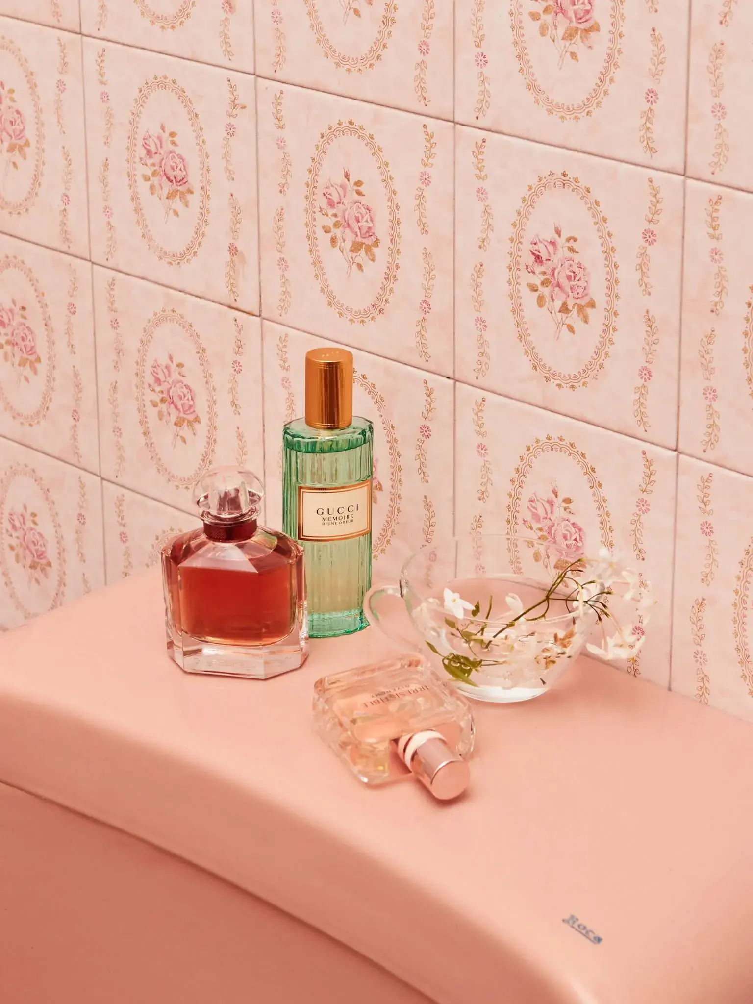 Bodegón de perfumes con estética vintage sobre fondo rosa.